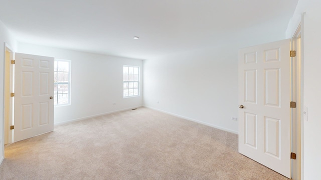 empty room featuring baseboards and light carpet