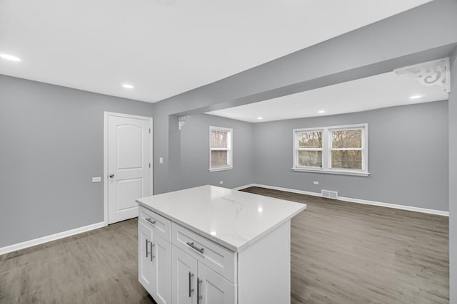 kitchen with light wood-style floors, white cabinets, visible vents, a kitchen island, and baseboards