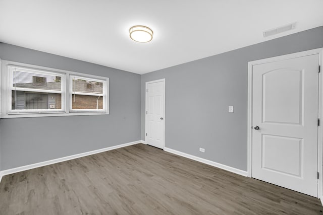 unfurnished bedroom with wood finished floors, baseboards, a closet, and visible vents