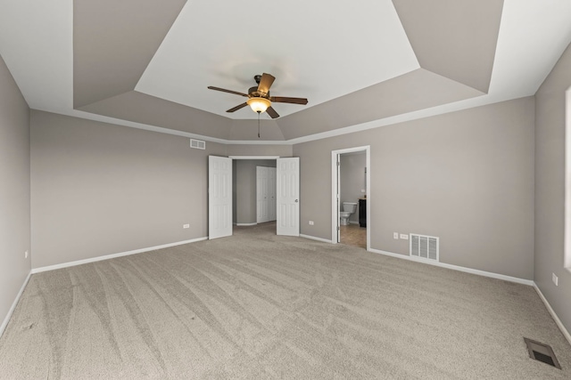 unfurnished bedroom with carpet flooring, visible vents, a tray ceiling, and baseboards