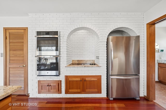 kitchen featuring brown cabinetry, wood finished floors, light stone countertops, and stainless steel appliances