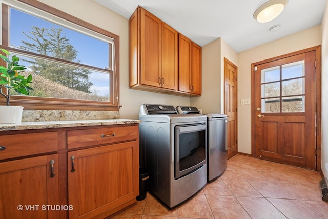 clothes washing area featuring light tile patterned floors, washer and clothes dryer, baseboards, and cabinet space