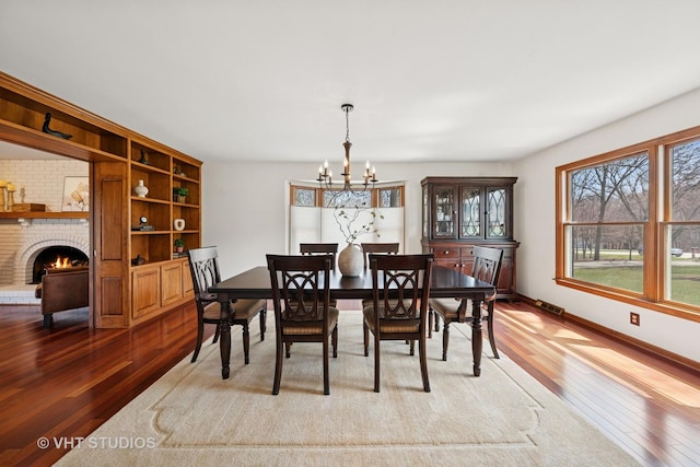 dining room with a fireplace, hardwood / wood-style floors, baseboards, and an inviting chandelier