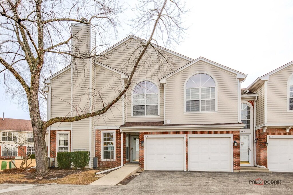multi unit property with a chimney, brick siding, aphalt driveway, and an attached garage
