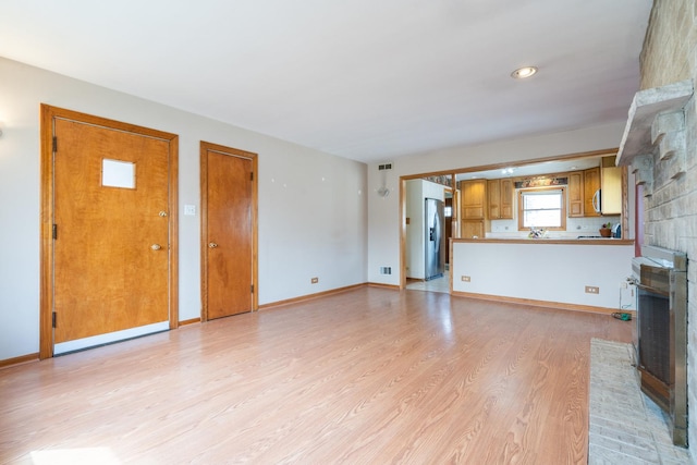 unfurnished living room with light wood finished floors, baseboards, and a fireplace
