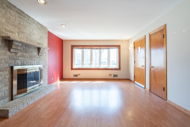 unfurnished living room with a brick fireplace, visible vents, baseboards, and wood finished floors