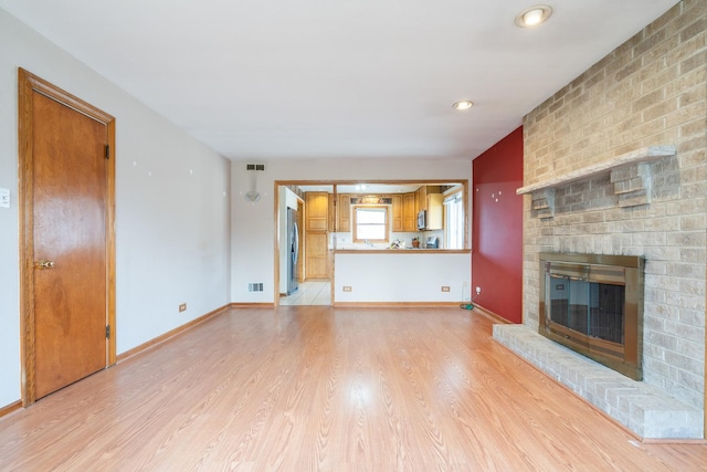 unfurnished living room featuring a fireplace, baseboards, light wood finished floors, and visible vents