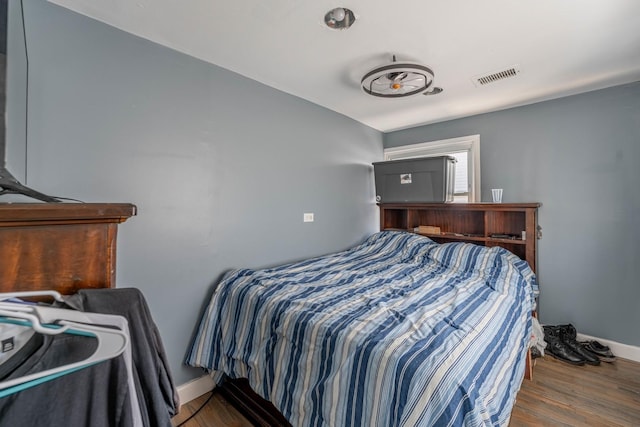 bedroom with baseboards, visible vents, and wood finished floors