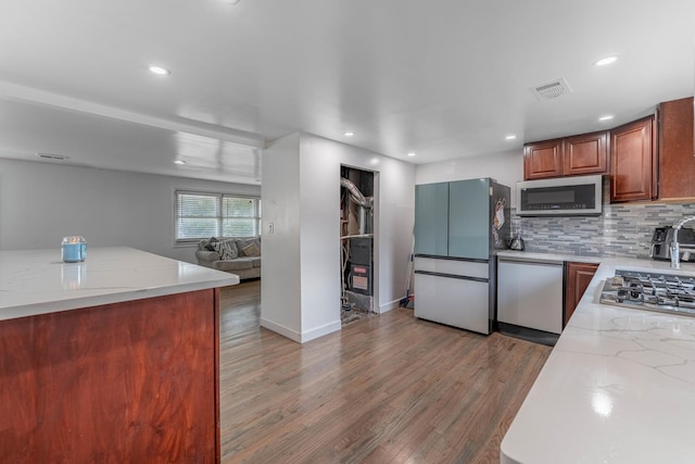 kitchen with tasteful backsplash, light wood-type flooring, stainless steel appliances, light stone counters, and visible vents