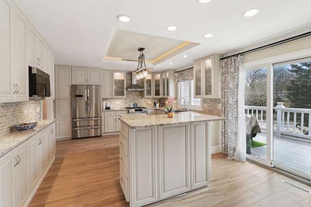 kitchen with a tray ceiling, tasteful backsplash, appliances with stainless steel finishes, and wall chimney range hood
