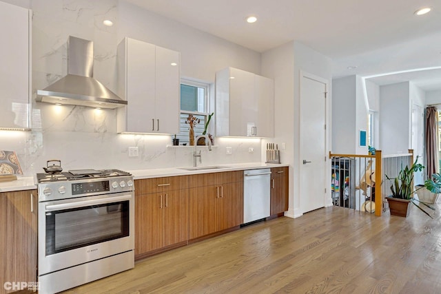 kitchen with stainless steel appliances, light wood finished floors, wall chimney exhaust hood, and a sink