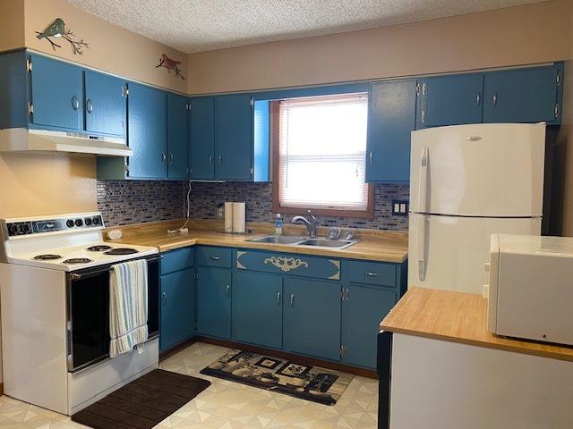 kitchen featuring blue cabinetry, a sink, under cabinet range hood, and white appliances