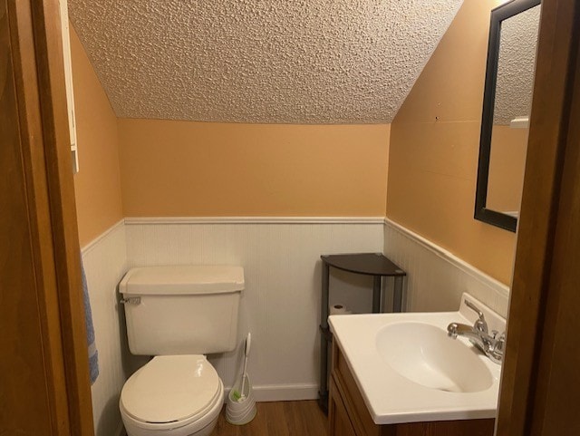 bathroom with toilet, wood finished floors, vanity, vaulted ceiling, and wainscoting