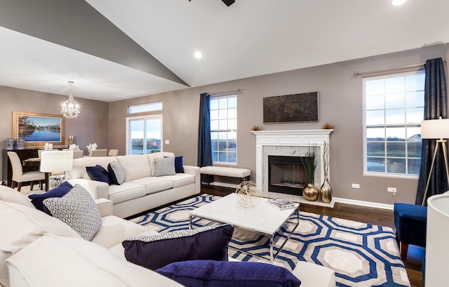 living room featuring a fireplace, vaulted ceiling, wood finished floors, baseboards, and a notable chandelier