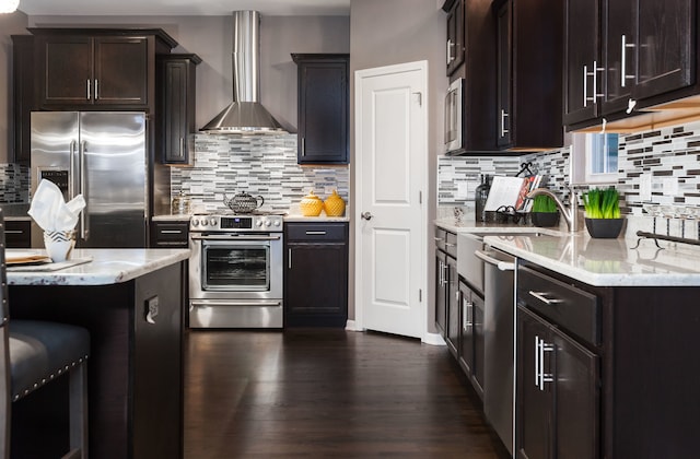 kitchen with stainless steel appliances, tasteful backsplash, light stone counters, and wall chimney range hood