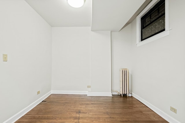 spare room featuring radiator heating unit, dark wood-style flooring, and baseboards