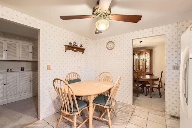 dining space with ceiling fan with notable chandelier, wallpapered walls, and light tile patterned floors