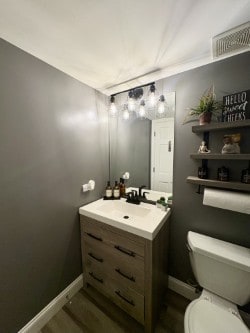 half bath featuring baseboards, wood finished floors, toilet, and vanity