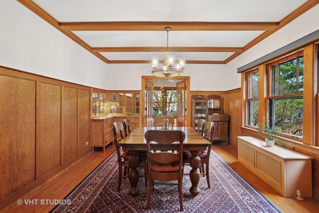 dining room with an inviting chandelier, crown molding, beam ceiling, light wood finished floors, and wainscoting