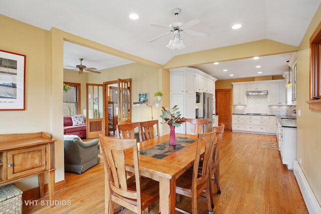 dining space with a baseboard heating unit, light wood-style flooring, vaulted ceiling, and a ceiling fan