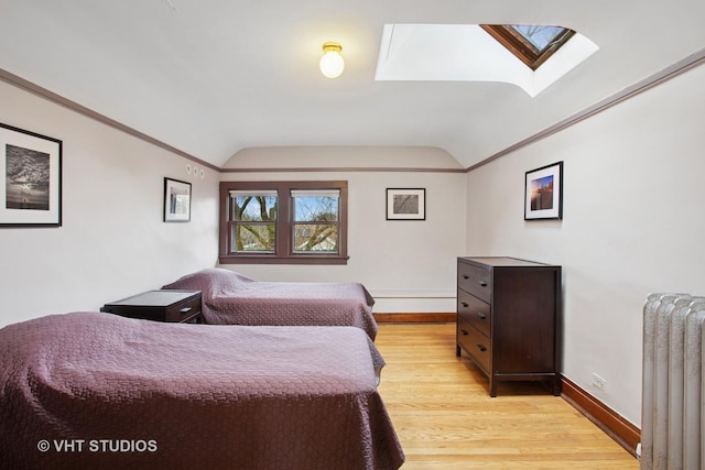bedroom featuring vaulted ceiling with skylight, baseboards, ornamental molding, radiator, and light wood-style flooring