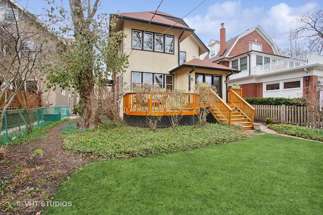 rear view of house with stucco siding, a chimney, a deck, fence, and a lawn