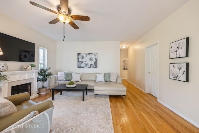 living room featuring a ceiling fan, baseboards, a glass covered fireplace, and light wood-style flooring