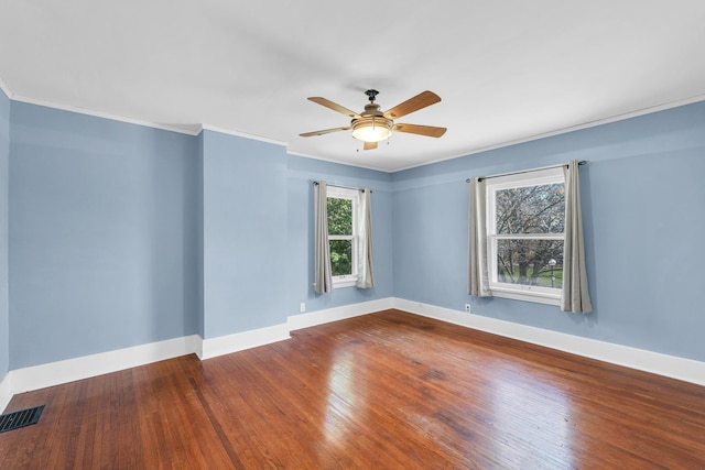 spare room with wood-type flooring, visible vents, baseboards, and ornamental molding
