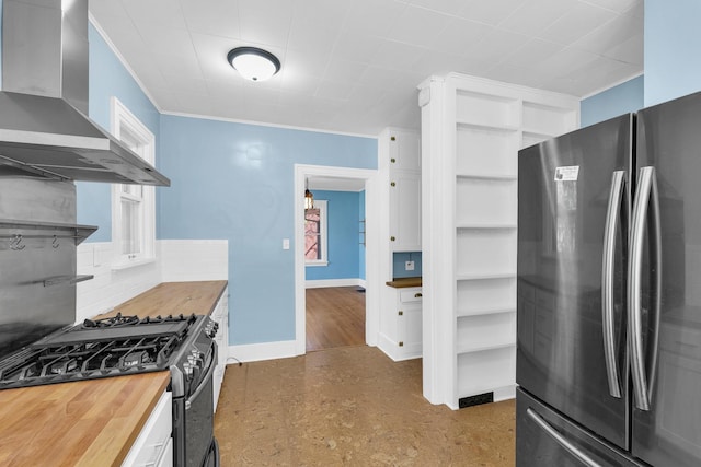 kitchen featuring butcher block counters, wall chimney range hood, appliances with stainless steel finishes, baseboards, and backsplash