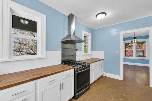 kitchen featuring tasteful backsplash, butcher block countertops, baseboards, wall chimney range hood, and stainless steel range with gas cooktop