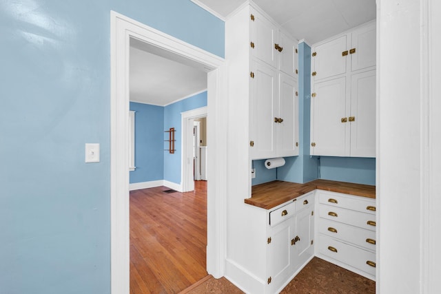 interior space with baseboards, dark wood-style flooring, wooden counters, crown molding, and white cabinetry