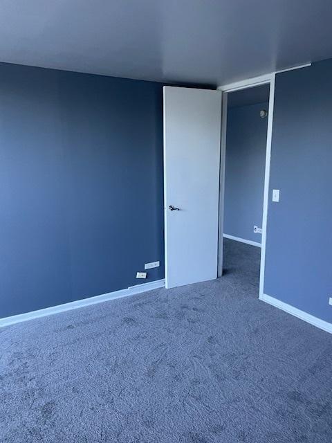 empty room with baseboards and dark colored carpet
