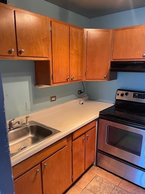 kitchen with light tile patterned flooring, light countertops, a sink, under cabinet range hood, and stainless steel electric range oven