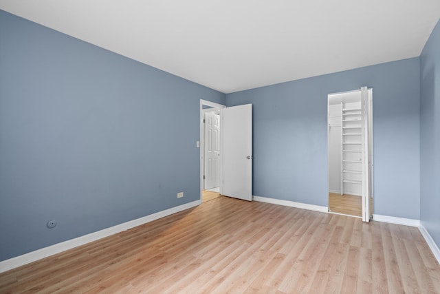 unfurnished bedroom featuring baseboards, a spacious closet, a closet, and light wood finished floors