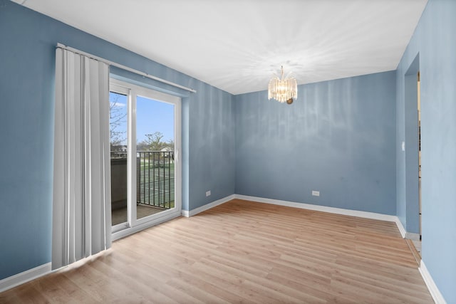unfurnished room featuring baseboards, wood finished floors, and an inviting chandelier