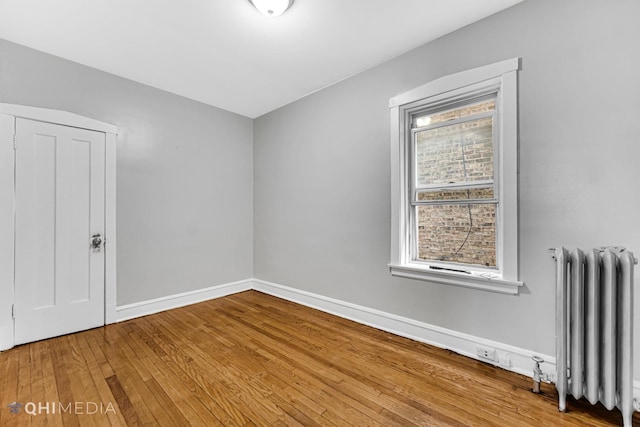 spare room featuring radiator heating unit, baseboards, and wood-type flooring
