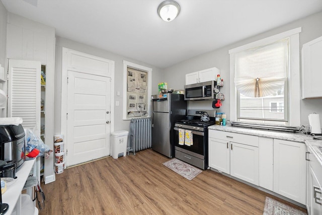 kitchen with light wood-style floors, appliances with stainless steel finishes, light stone counters, and white cabinetry