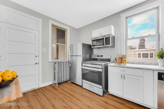 kitchen featuring light wood-style floors, radiator, stainless steel appliances, baseboards, and white cabinetry