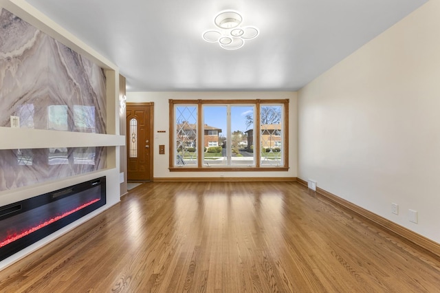 unfurnished living room with wood finished floors, baseboards, and a glass covered fireplace