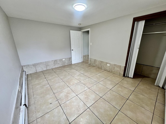unfurnished bedroom with light tile patterned floors, a closet, and a baseboard radiator