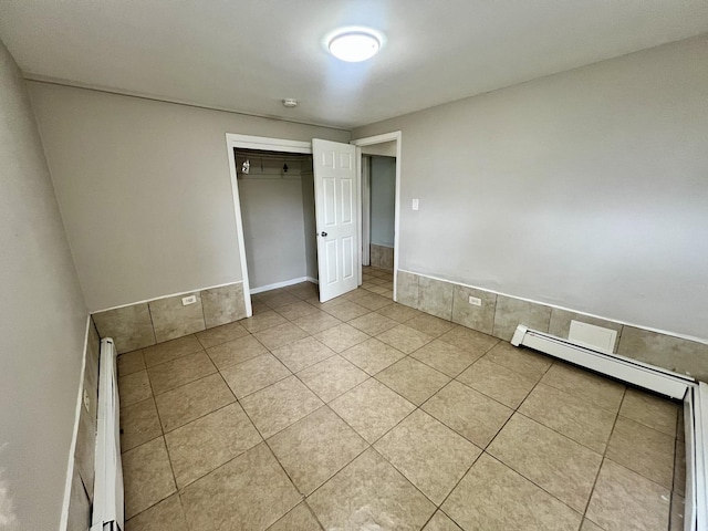 unfurnished bedroom featuring light tile patterned floors, a closet, and a baseboard radiator