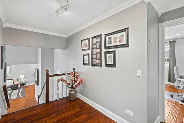 corridor featuring wood finished floors, rail lighting, an upstairs landing, crown molding, and baseboards
