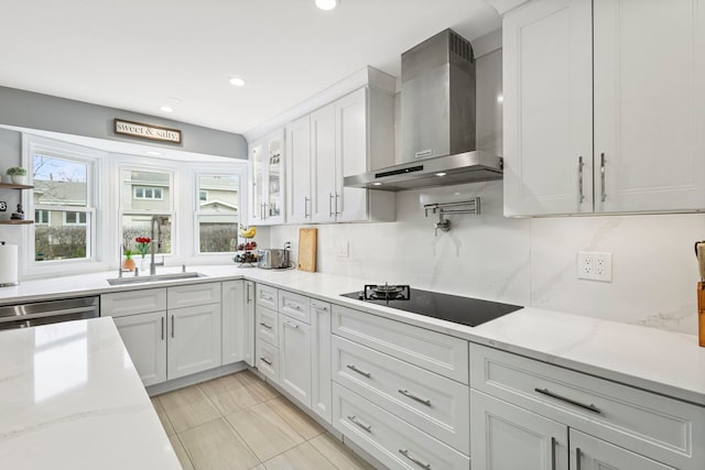 kitchen featuring wall chimney range hood, stainless steel dishwasher, a sink, black electric stovetop, and white cabinetry