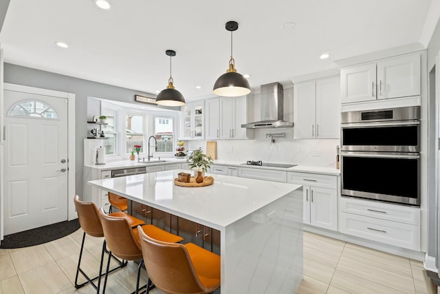 kitchen with white cabinets, stainless steel appliances, light countertops, wall chimney range hood, and a sink