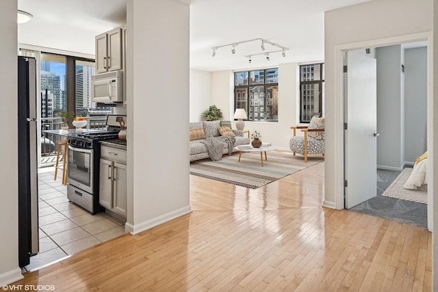 kitchen featuring stainless steel gas range, white microwave, freestanding refrigerator, track lighting, and light wood-style floors
