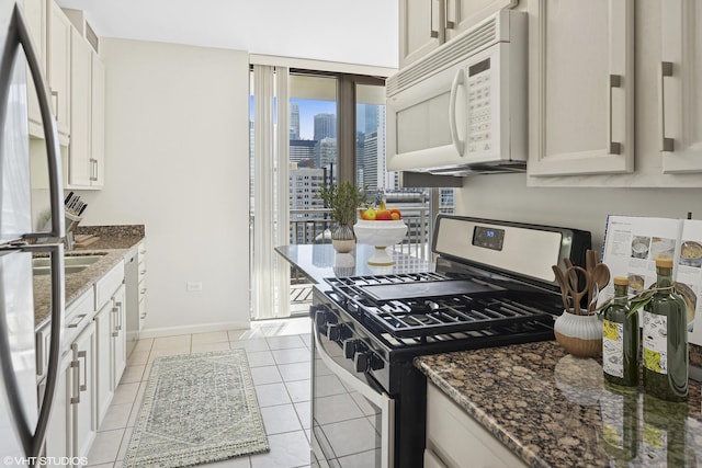 kitchen with appliances with stainless steel finishes, a view of skyline, dark stone countertops, light tile patterned flooring, and baseboards
