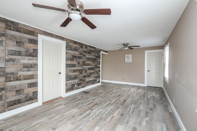 unfurnished room featuring an accent wall, a ceiling fan, wooden walls, wood finished floors, and baseboards
