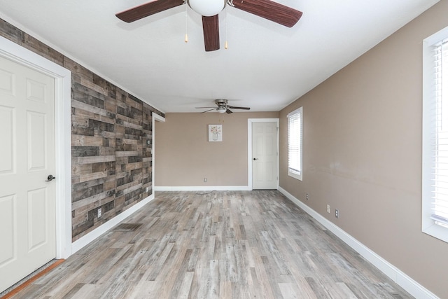spare room featuring an accent wall, a ceiling fan, wooden walls, light wood-type flooring, and baseboards