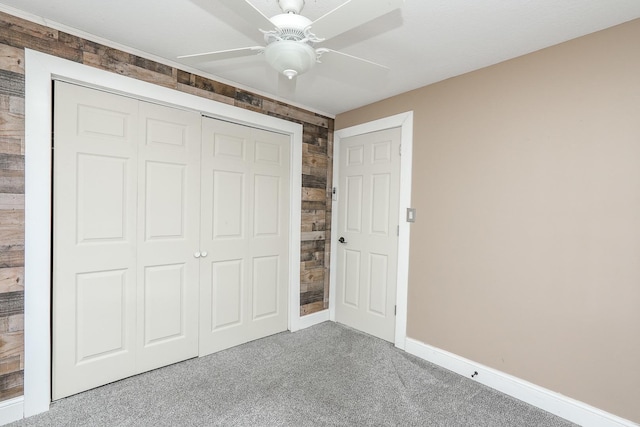 unfurnished bedroom featuring a closet, wooden walls, baseboards, a ceiling fan, and carpet floors