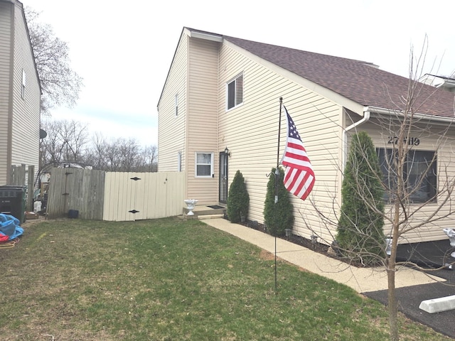 view of side of home with a shingled roof, a lawn, and a gate